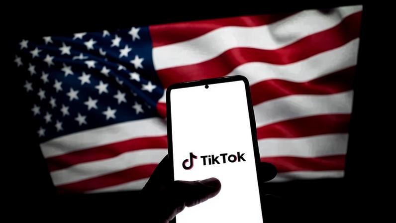 Foto de um celular com o logo do TikTok em frente à bandeira dos Estados Unidos