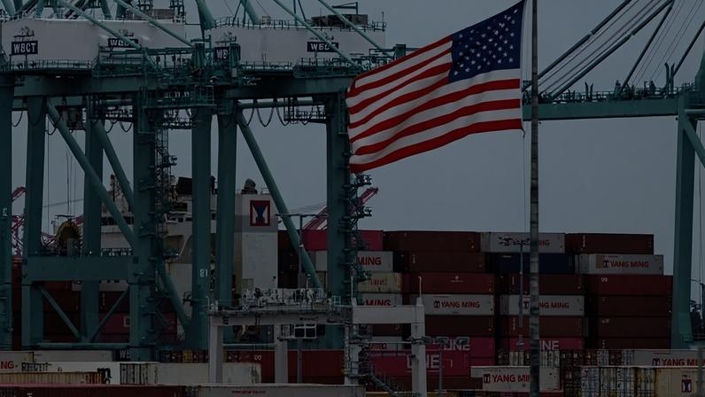 Uma bandeira dos EUA tremula perto de contêineres enquanto um navio e descarregado no Porto de Los Angeles