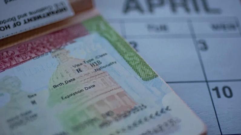 H1B visa (for specialty workers) stamp in passport, blurred april calendar on background. H1B visa program deadline concept. Close up view. (Getty Images)