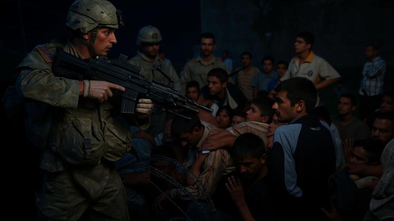 A U.S. soldier with an automatic rifle stands on one side of a barbed-wire fence and points the weapon into a crowd of people on the other side. Many in the crowd reach their open hands out. Other soldiers stand nearby in camouflage fatigues with their own weapons.