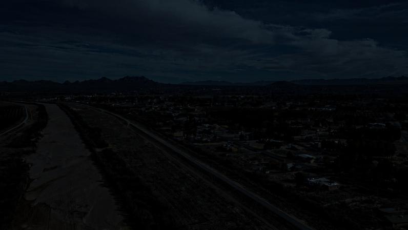 A brown river bed runs beneath a blue sky and dark mountains.