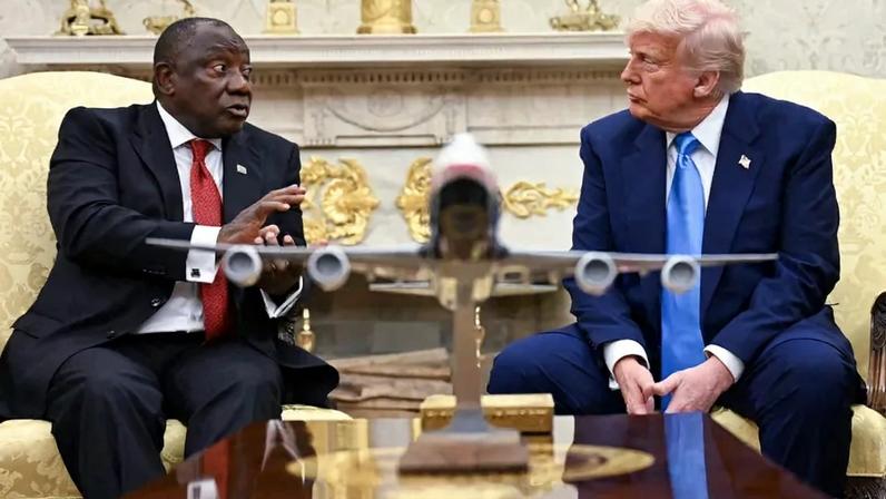 Ramaphosa (left) and Trump (right) look at each other as they engage in a discussion. Between them is a table with a model plane on it.
