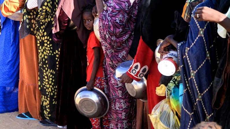 People line up with bowls in their hands. One girl in line looks toward the camera.
