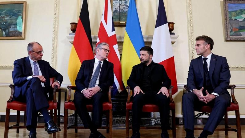 All four men sit on matching chairs in front of the flags of their respective countries, side by side, with their feet resting on the border of an ornate rug. Starmer and Zelensky's eyes are locked; the other two watch intently from either side.