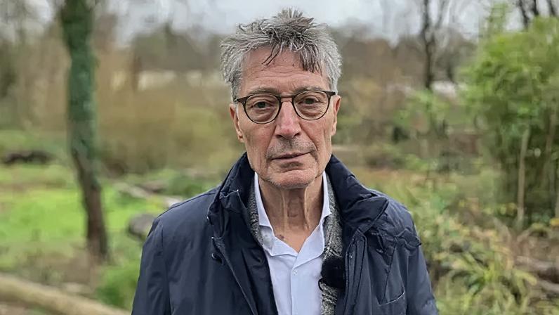 Kirk England/BBC Dirk Lips has a blue jacket and an open necked white shirt. He is wearing glasses and is looking directly at the camera.