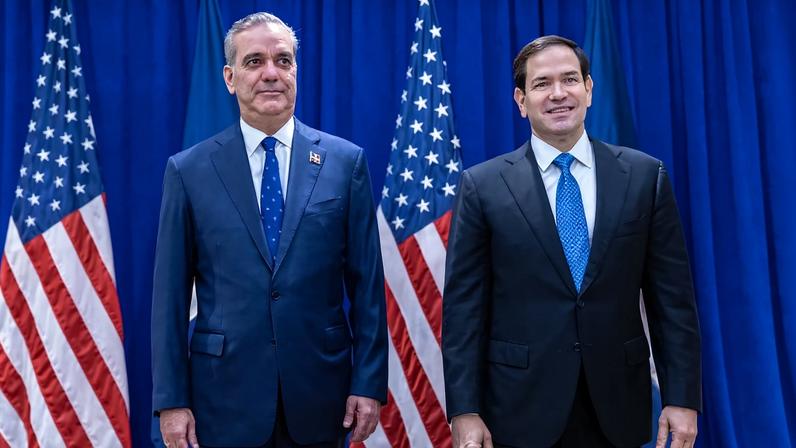 U.S. Secretary of State Marco Rubio and Dominican President Luis Abinader, both wearing suits, stand in front of two U.S. flags.