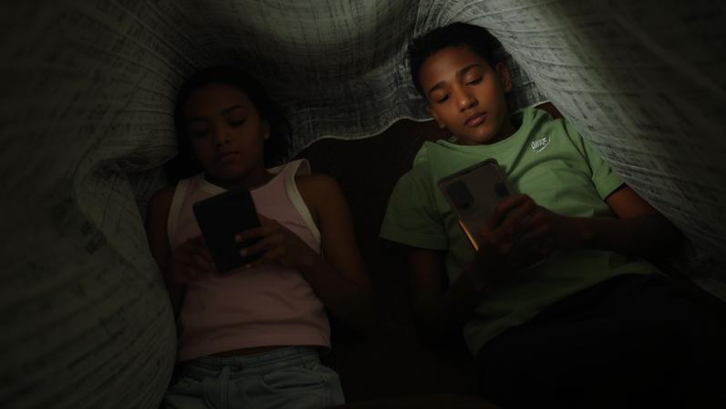 Os irmãos Clara Santana (10) e Pedro Santana (13), são vistos com celular na mão embaixo de um cobertor. Uma a cada 3 crianças tem perfil aberto em redes, alerta pesquisa Dados foram divulgados nesta terça pela Unico e Instituto Locomotiva Foto: Joédson Alves/Agência Brasil