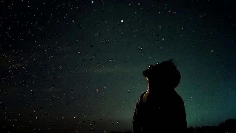 Fotografia de uma homem olhando para o céu noturno e observando as estrelas.