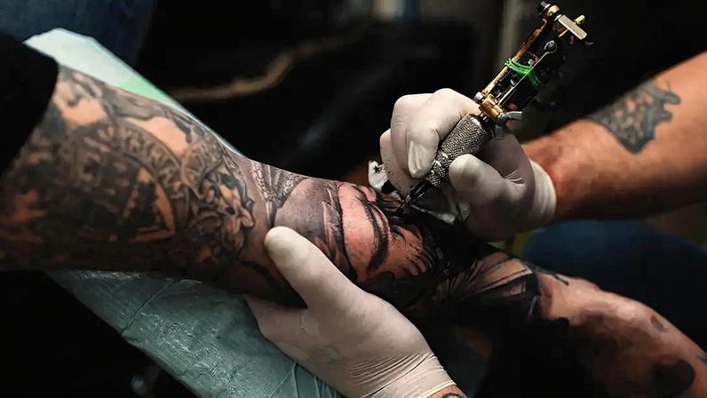 Fotografia de um Tatuador tatuando o braço de um jovem.
