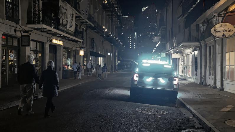 A couple walks at nighttime down a street illuminated by the blue lights of a police vehicle.
