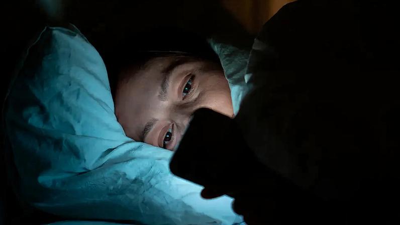 Fotografia de uma mulher deitada vidrada no celular.