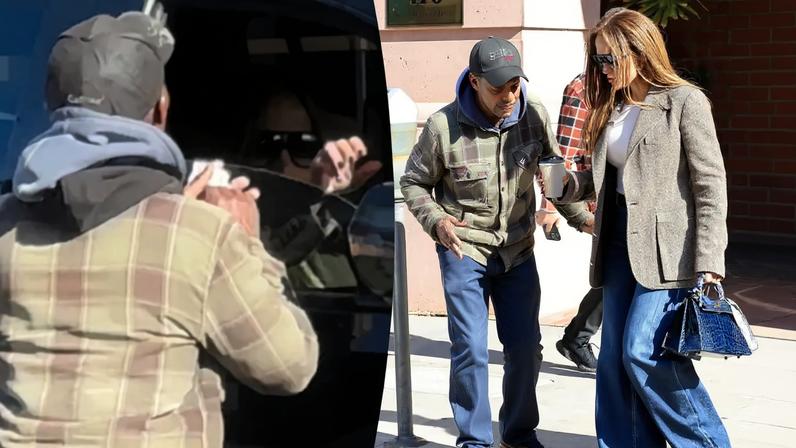 Jennifer Lopez in a tweed blazer and jeans, holding a blue handbag and a coffee cup, walks past a man in a plaid jacket.