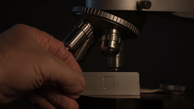 Fotografia de uma mão usando um microscópio.