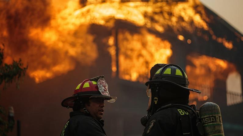 Firefighters stand in front of a burning building in the aftermath of a forest fire in the Biobio region where, according to local media, multiple wildfires prompted emergency evacuations, in Concepcion, Chile, January 18, 2026. REUTERS/Juan Gonzalez