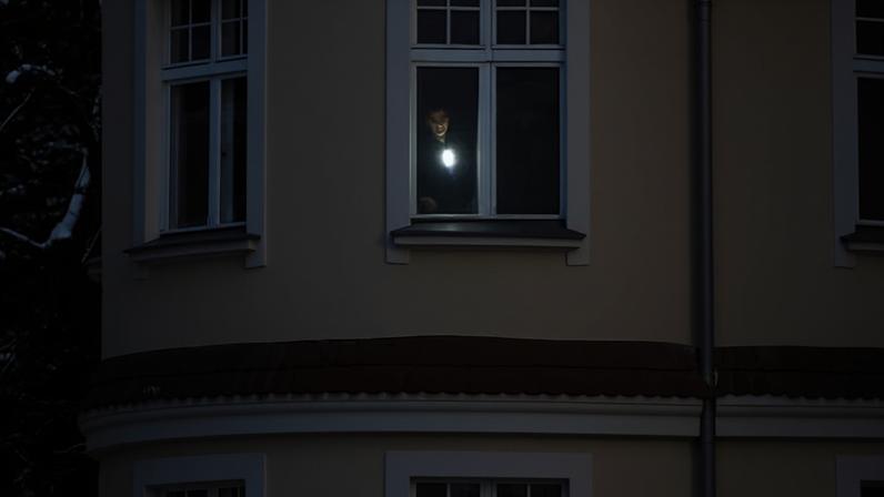 View from outside the building of a man standing at a window shining his torch from inside a dark room