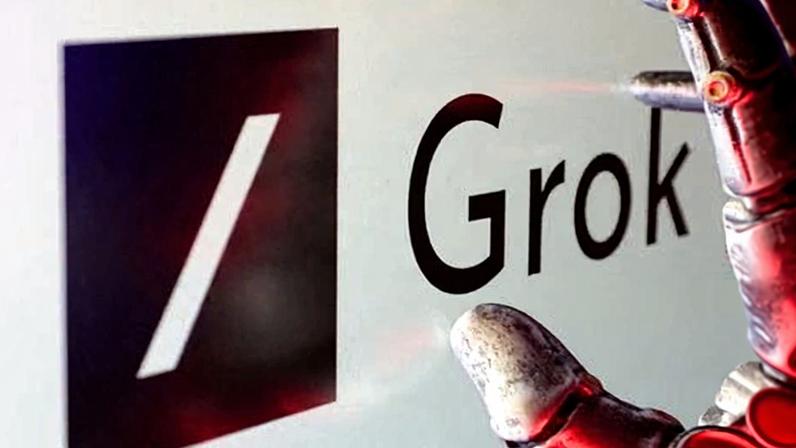 Robotic hand touching screen displaying Grok logo.
