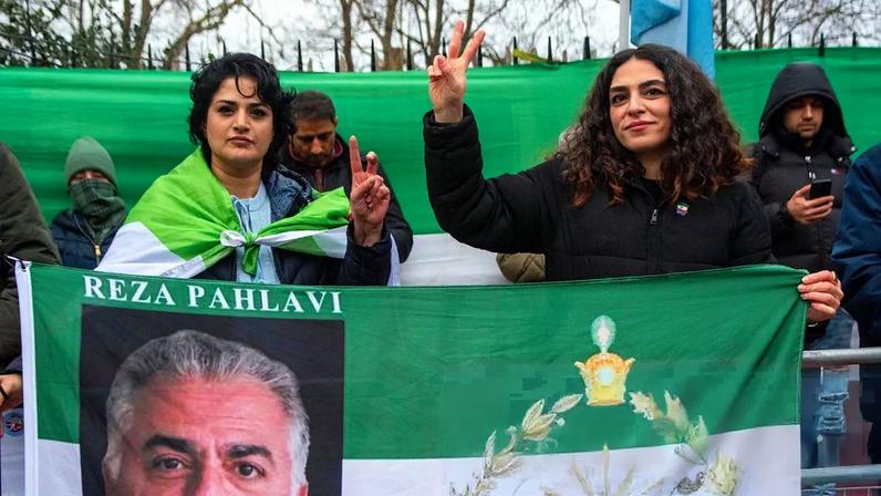 Two protesters show the sign of victory and hold a flag with Reza Pahlavi, son of Iran’s deposed shah, on it during the demonstration outside the Iranian Embassy in London. Follow the latest developments, live.