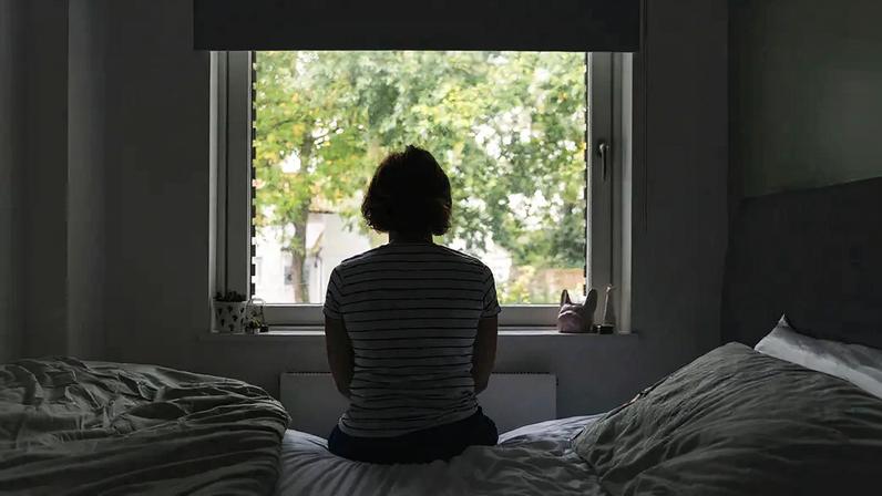 Fotografia de costas de uma mulher olhando pela janela do quarto.