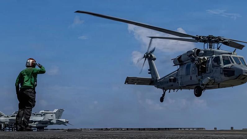 A US officer signals to a carrier an MH-60R Sea Hawk helicopter