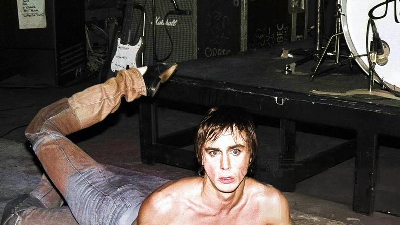 Iggy Pop lies on the stage, microphone in hand
