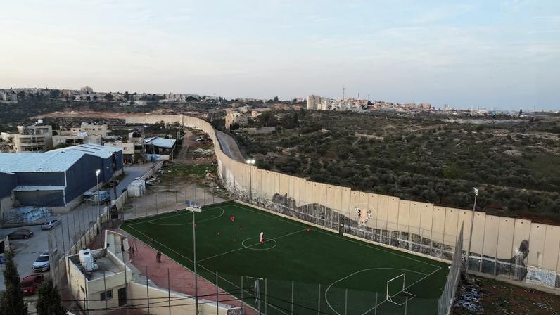 Drone view shows a man dressed as Santa playing football with Palestinian teens next to West Bank barrier separating Aida refugee camp from Jerusalem, in the Israeli-occupied city of Bethlehem, December 22, 2025. REUTERS/Ammar Awad