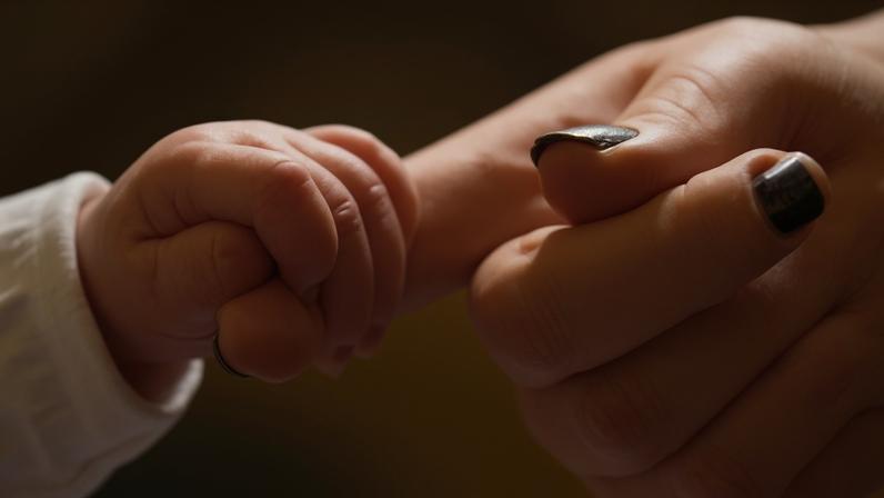 The hand of a new baby holding the finger of its mother