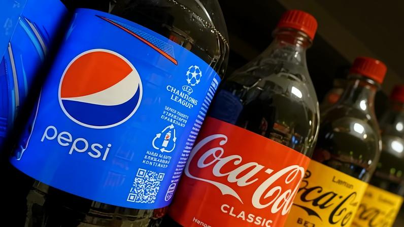 Bottles of Pepsi and Coca-Cola sit side by side in a supermarket