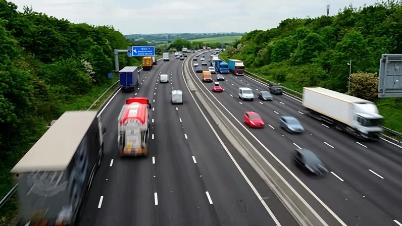 Traffic speeds in both directions on a four-lane motorway; the cars and lorries are blurred. A blue sign ahead indicates the exit for the A57 to Sheffield and Rotherham.