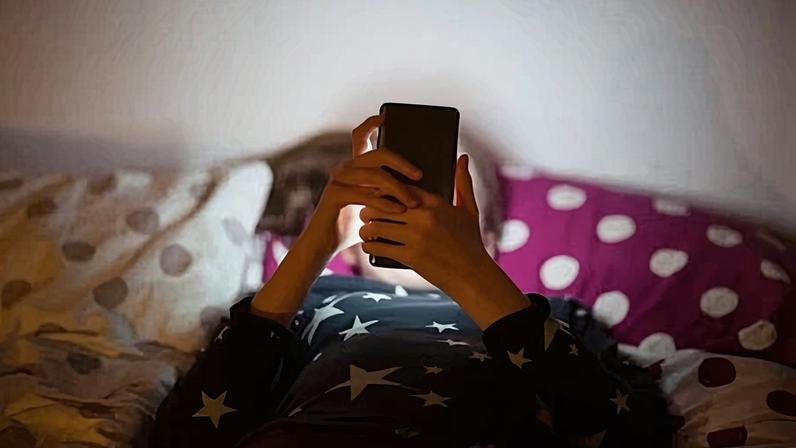 Girl lying on bed at night and using a mobile phone