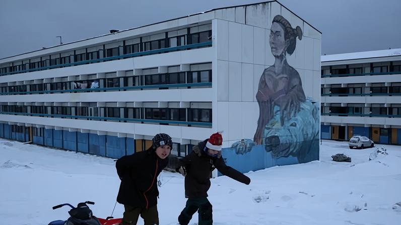 Children pull sleds through snow next to residential apartment buildings Nuuk, Greenland.