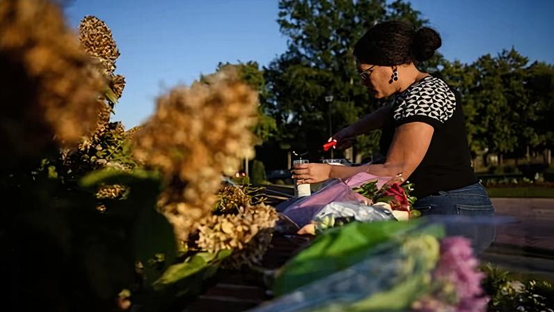 A person lays flowers and lights candles at the entrance of Hedingham neighborhood in Raleigh, North Carolina, on 14 October 2022, after five people were killed.