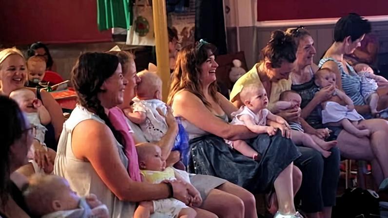 Women holding babies watching a performance - some of them are laughing and some are tending to their children.