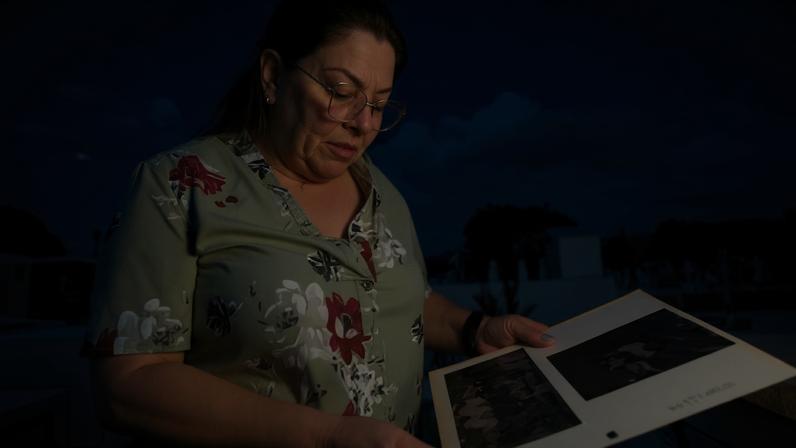 Woman in cemetery, looking at pictures on page taken out of photo album.