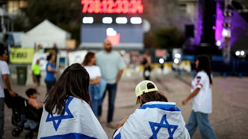 Women wrapped in Israeli flags stand in front of a clock counting the days since the deadly October 7, 2023, Hamas attack, at "Hostages Square" in Tel Aviv, Israel, October 14, 2025, following the release of hostages after a ceasefire between Israel and Hamas went into effect.