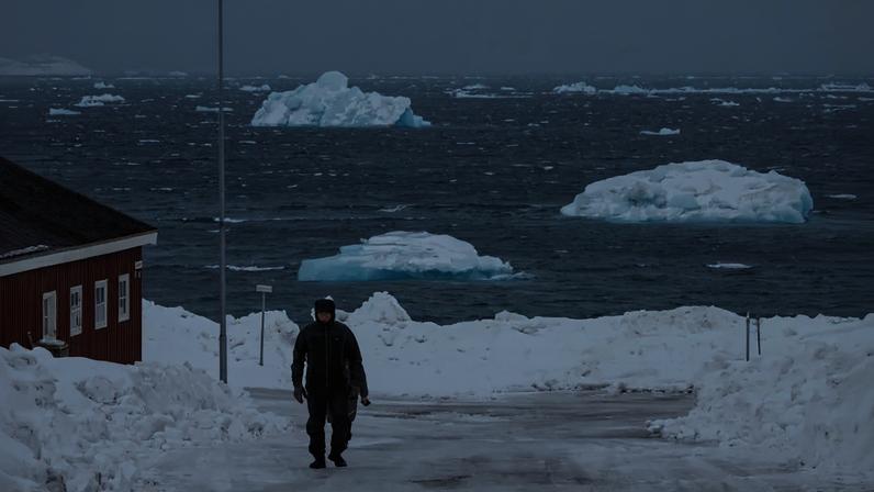 Icebergs are seen in the sea as a man walks along a road in Nuuk, Greenland, on March 9, 2025.