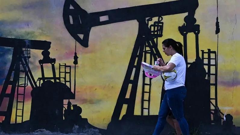 A woman walks past a mural depicting an oil pump on a street in Caracas, Venezuela.