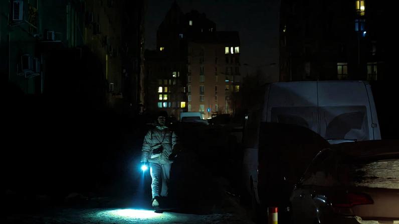 A man carries a torch as he walks in a dark street in a neighbourhood with an electricity outage in Kyiv