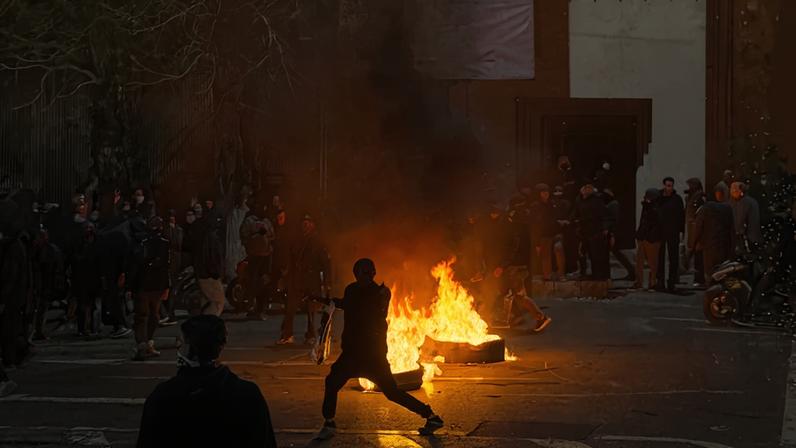 Iranians block a street in Tehran amid burning objects and heavy smoke.