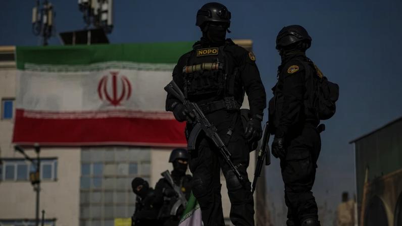 Iranian security forces hold guns while standing in front of an Iranian flag during a pro-government rally in Tehran.