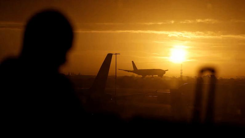 A passenger waits in departures as a British Airways plane lands at London Heathrow airport