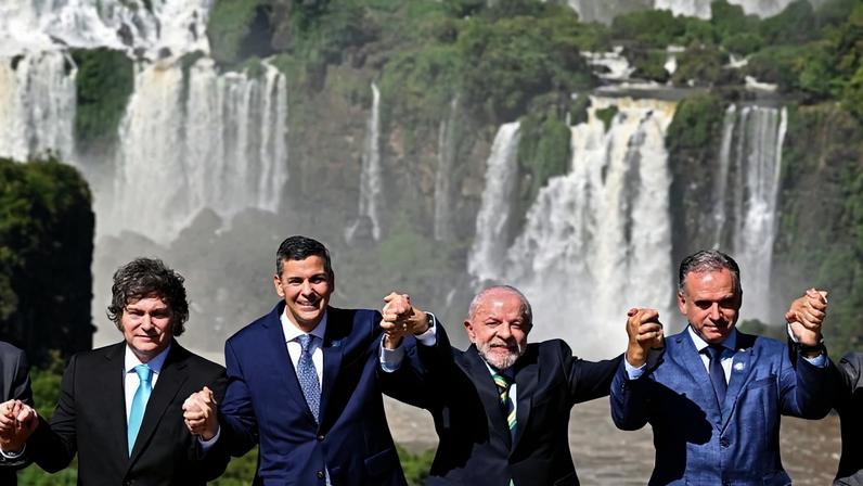 The president of Argentina, Paraguay, Brazil, and Uruguay stand holding hands in front of a waterfall.