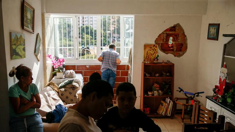 People sit inside a home where a wall was punctured by a rocket fragment, after the U.S. launched a strike on Venezuela, capturing its President Nicolas Maduro and his wife Cilia Flores, in Caracas, Venezuela January 4, 2026. REUTERS/Leonardo Fernandez Viloria/File Photo