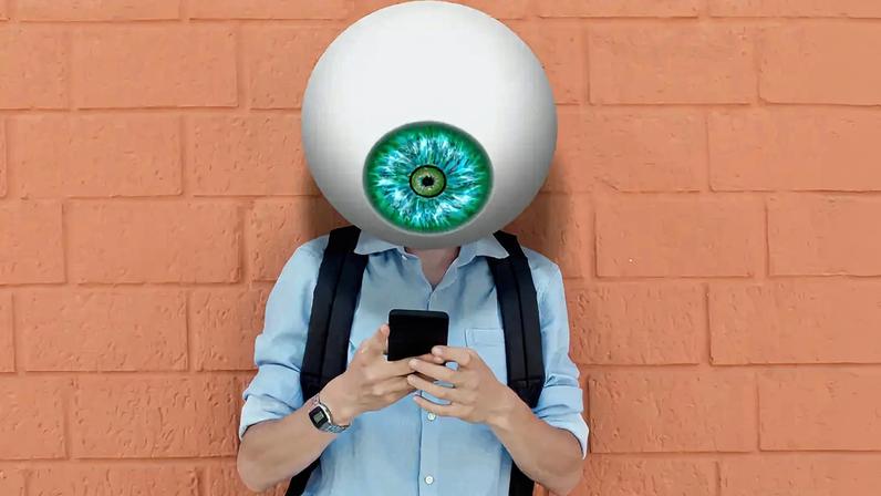 Imagem de um jovem com um gigantesco olho no lugar da cabeça checando o celular. Ao fundo, vê-se um muro de tijolos aparentes.