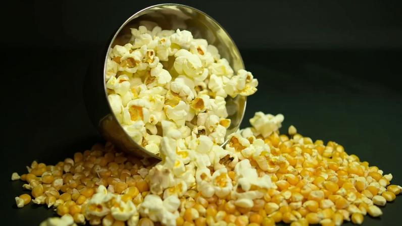 Imagem, em fundo preto, de pipocas sobre grãos de milho.