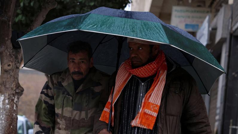 Men stand under an umbrella on a cold, rainy day in the Moroccan city of Fes