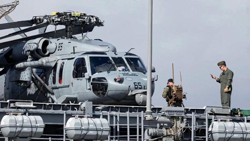 U.S. military personnel stand on the flight deck of the USS Iwo Jima (LHD-7) next to an MH-60S Seahawk helicopter while the ship is docked at the port of Ponce, Puerto Rico, on Jan. 15.