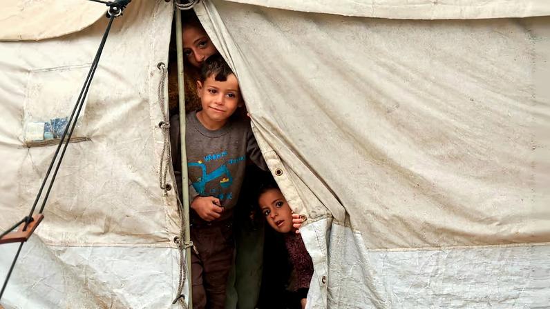 Displaced Palestinian children look out of a shelter in a tent camp on a rainy day in Khan Younis, southern Gaza Strip, December 11, 2025. REUTERS/Haseeb Alwazeer/File Photo