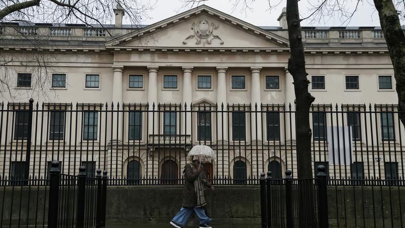 People shelter under umbrellas as they walk past the Royal Mint Court, the proposed site of the new Chinese embassy, in London