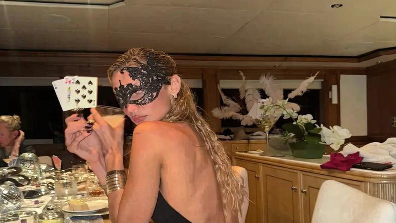 Bella Hadid in a vintage Jean Paul Gaultier dress and a masquerade mask holding playing cards and a drink.