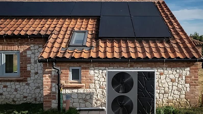 Andrew Aitchison/Getty Images Stone cottage with brown tiled roof, with a blue sky behind. The roof is covered in solar panels and to the right hand side of the cottage is a heat pump